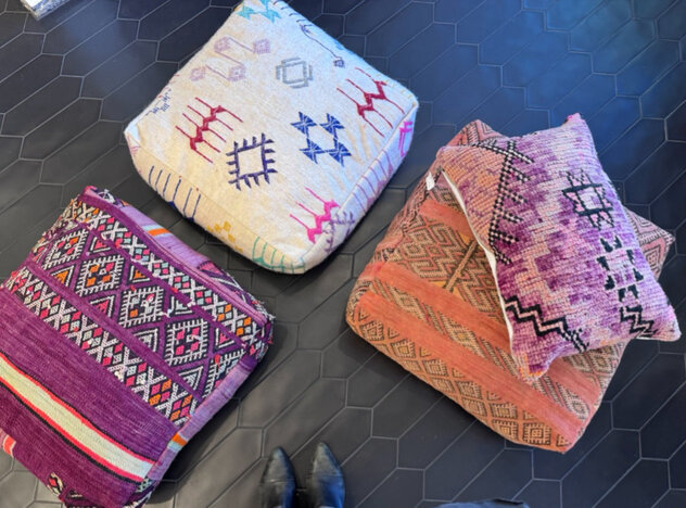 Three pouf pillows on the ground with a fourth pillow made from purple moroccan rug on top